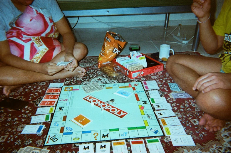 a close up of two people sitting on a floor playing monopoly