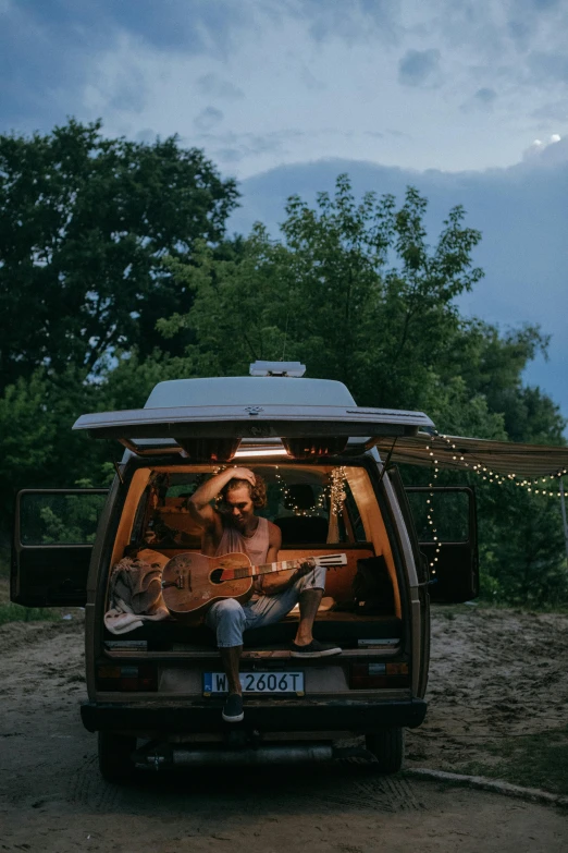 a guy in the back of a van sitting by the trees