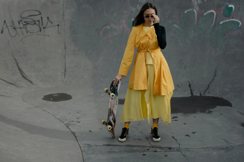 a young woman holding a skateboard while wearing a yellow coat