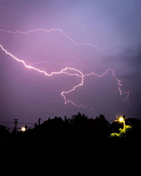 lightning flashes across the night sky behind a neighborhood