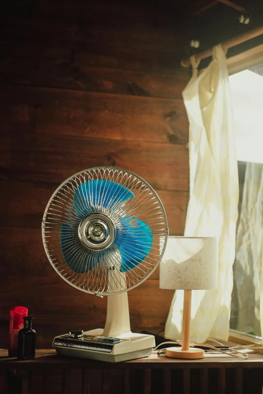 a table with a lamp, fan and book on it