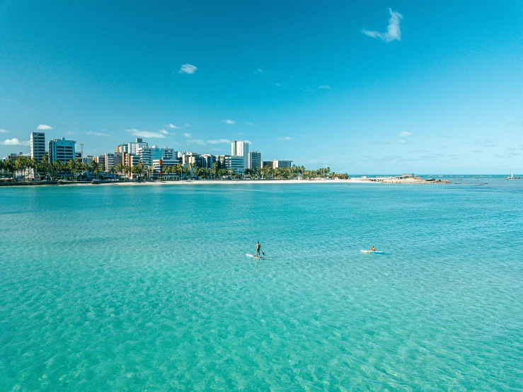 two people stand in the clear, blue water near a large city