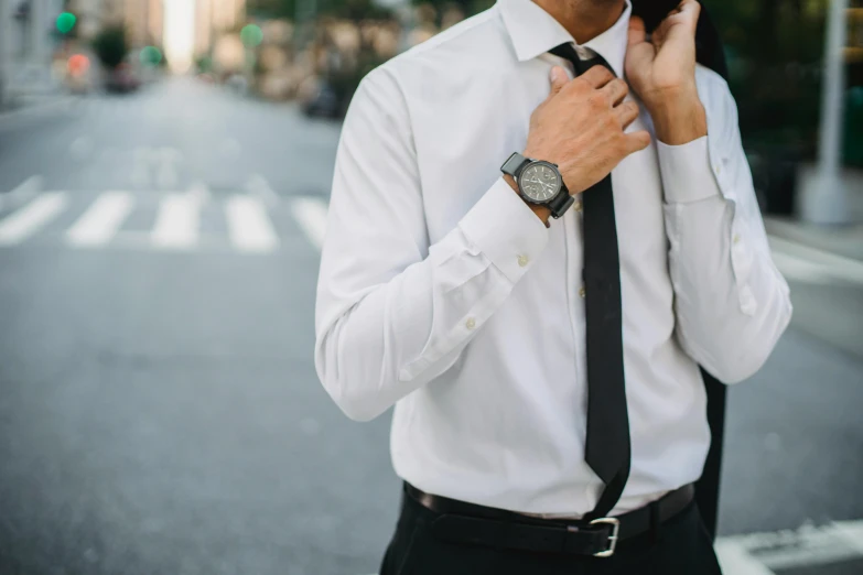 a man adjusts his tie while standing on the street