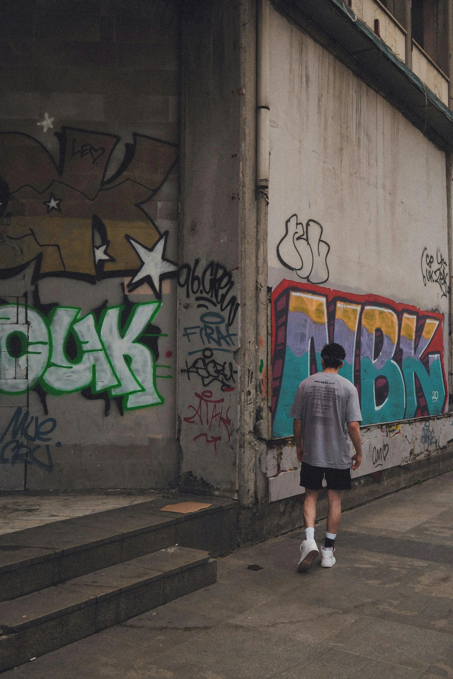 a man in grey shirt and white sneakers walking by grafitti