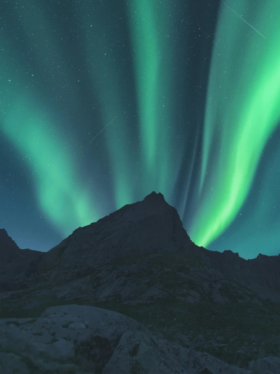 the aurora lights glow brightly green above a mountain top