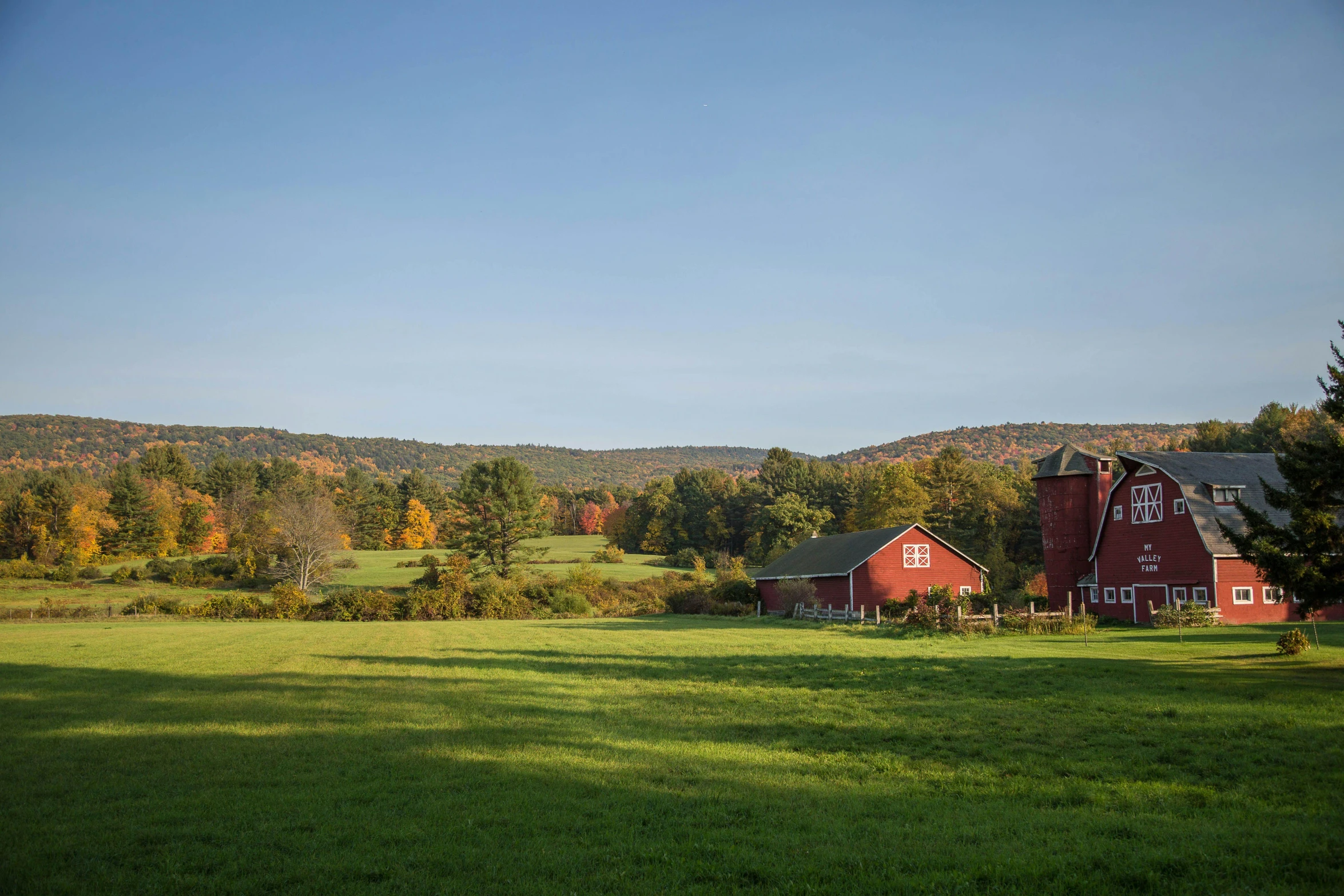 a farm with two red barns, one with autumn leaves on trees, and the other with fall foliage