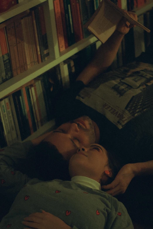 a boy and girl laying on the floor in front of a book shelf reading a book