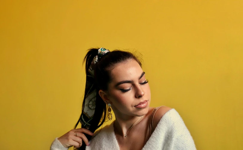a woman is holding her hair in the yellow background