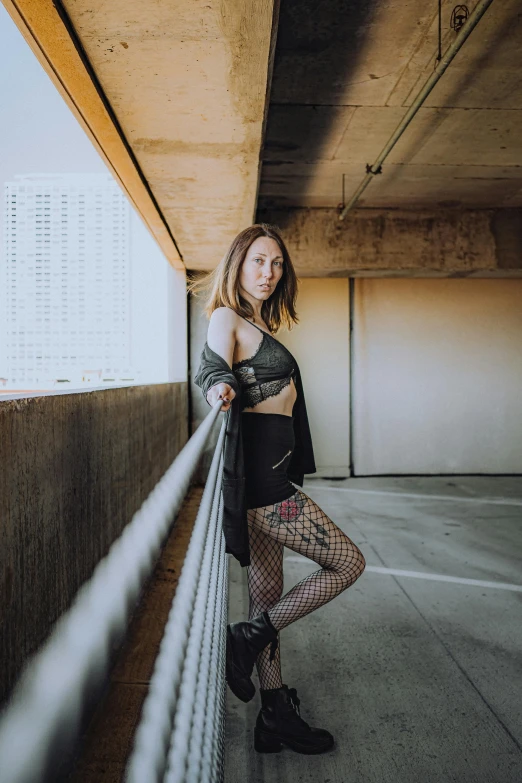 a woman with very big  wearing black and gray, leaning on the railing of an underpass