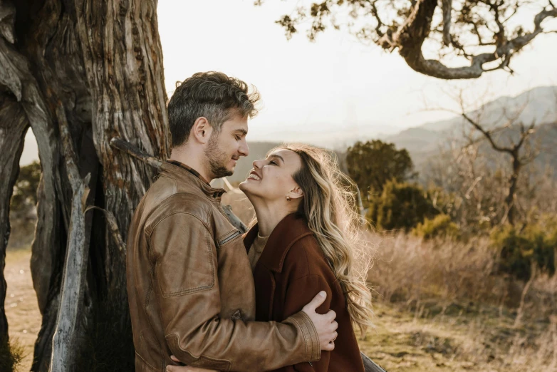 a couple emcing next to a tree in a field