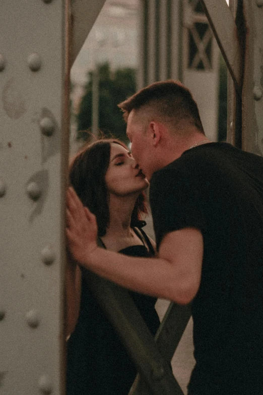 man and woman kissing and leaning against a rail