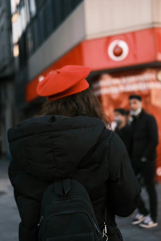 woman with a red cap and backpack walking down a street