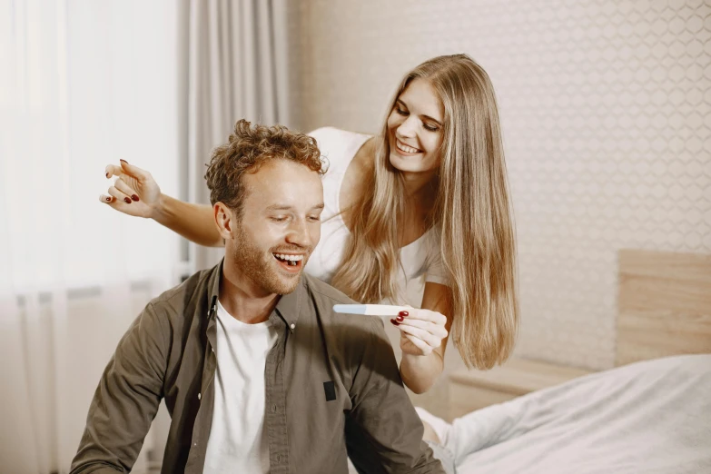 a smiling woman brushing a man's hair while he looks in the mirror