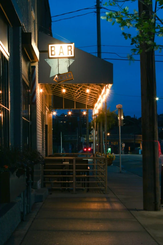 the entrance of a bar illuminated with lights and a red car parked in the distance