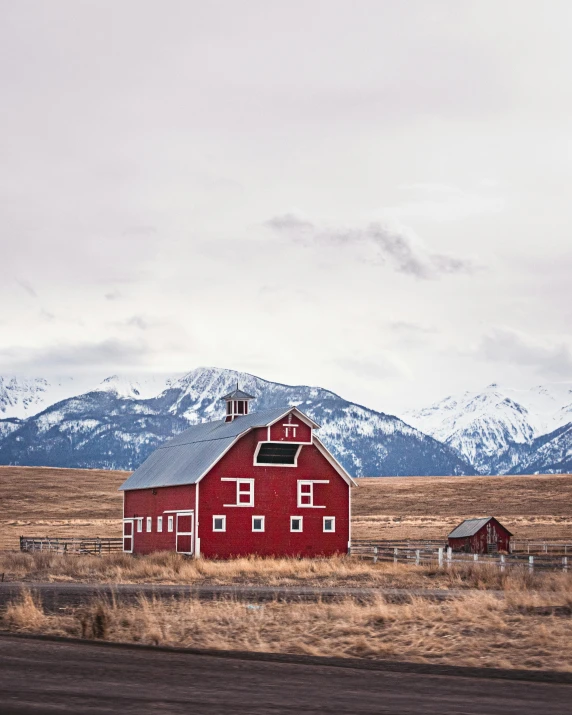 a barn and two barns in a field with snowy mountains in the background