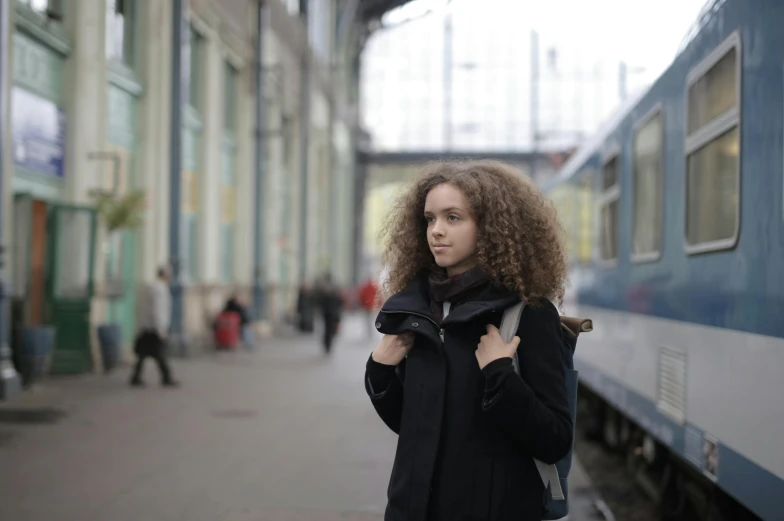 woman with long curly hair standing by train at station