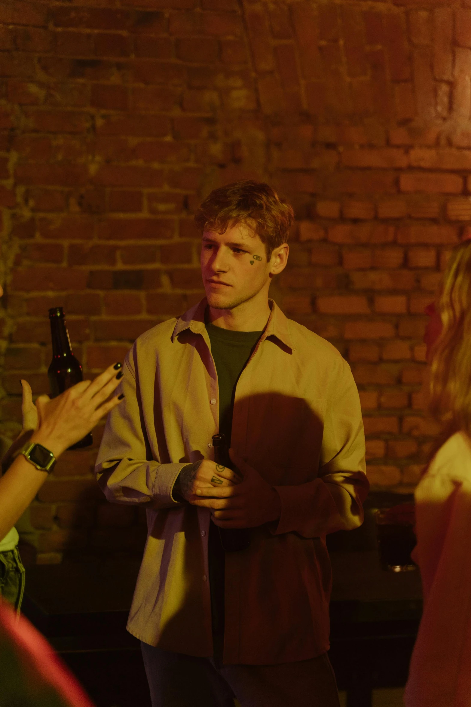 a man standing in a room next to a brick wall holding a bottle