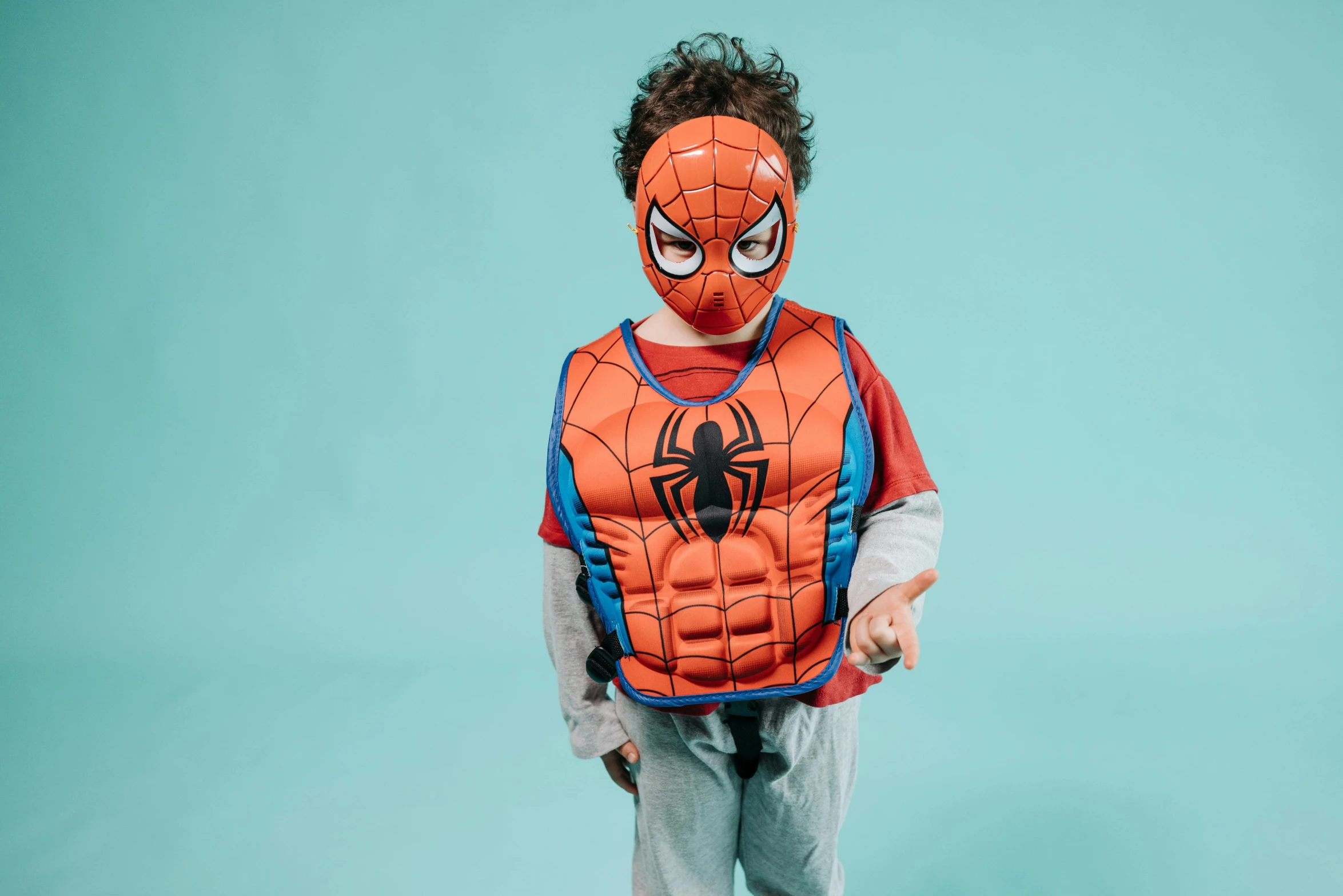 a boy wearing spider man clothes, holding his arms out