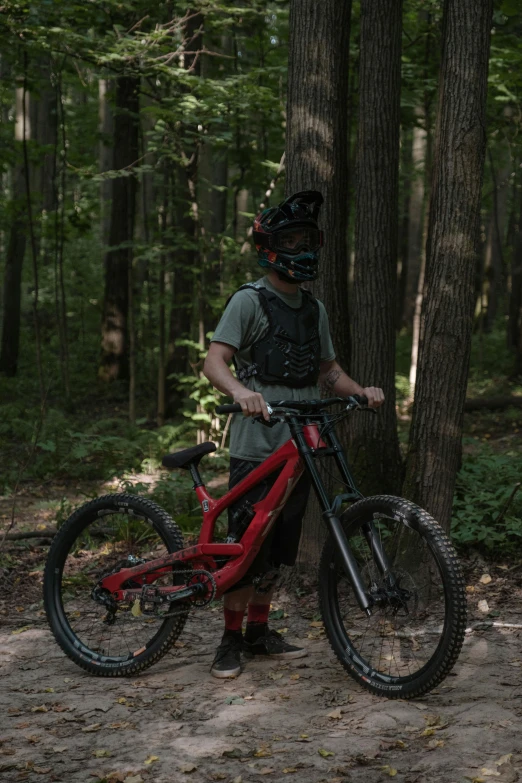 a man standing next to a red bike in the woods