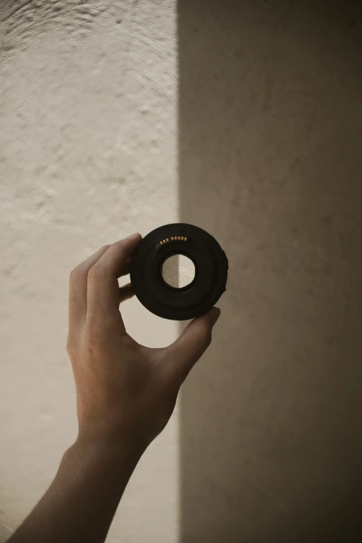 hand holding black object up against a wall