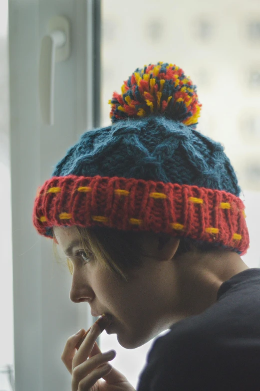 woman in blue and yellow knitted hat looking out window