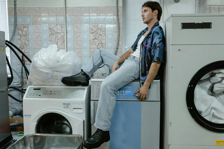 the man sits on top of a washing machine in a laundry room