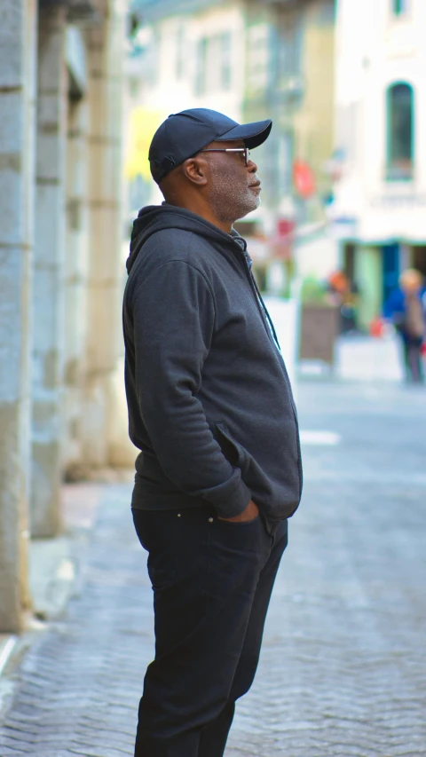 man in a black hat, hoodie and sweatpants standing outside a building