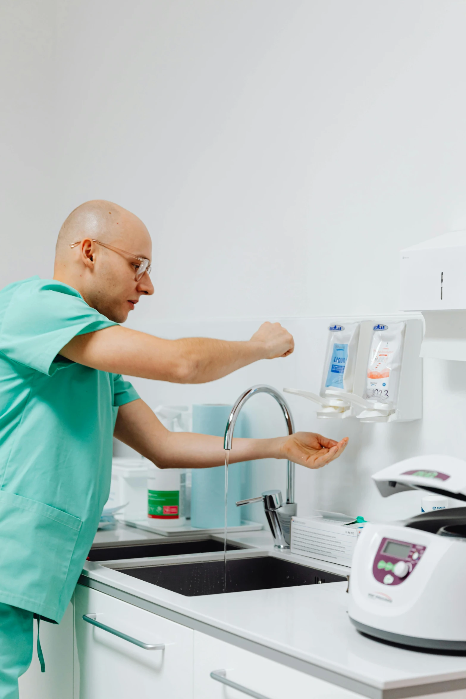 a man in green shirts is washing his hands under the sink