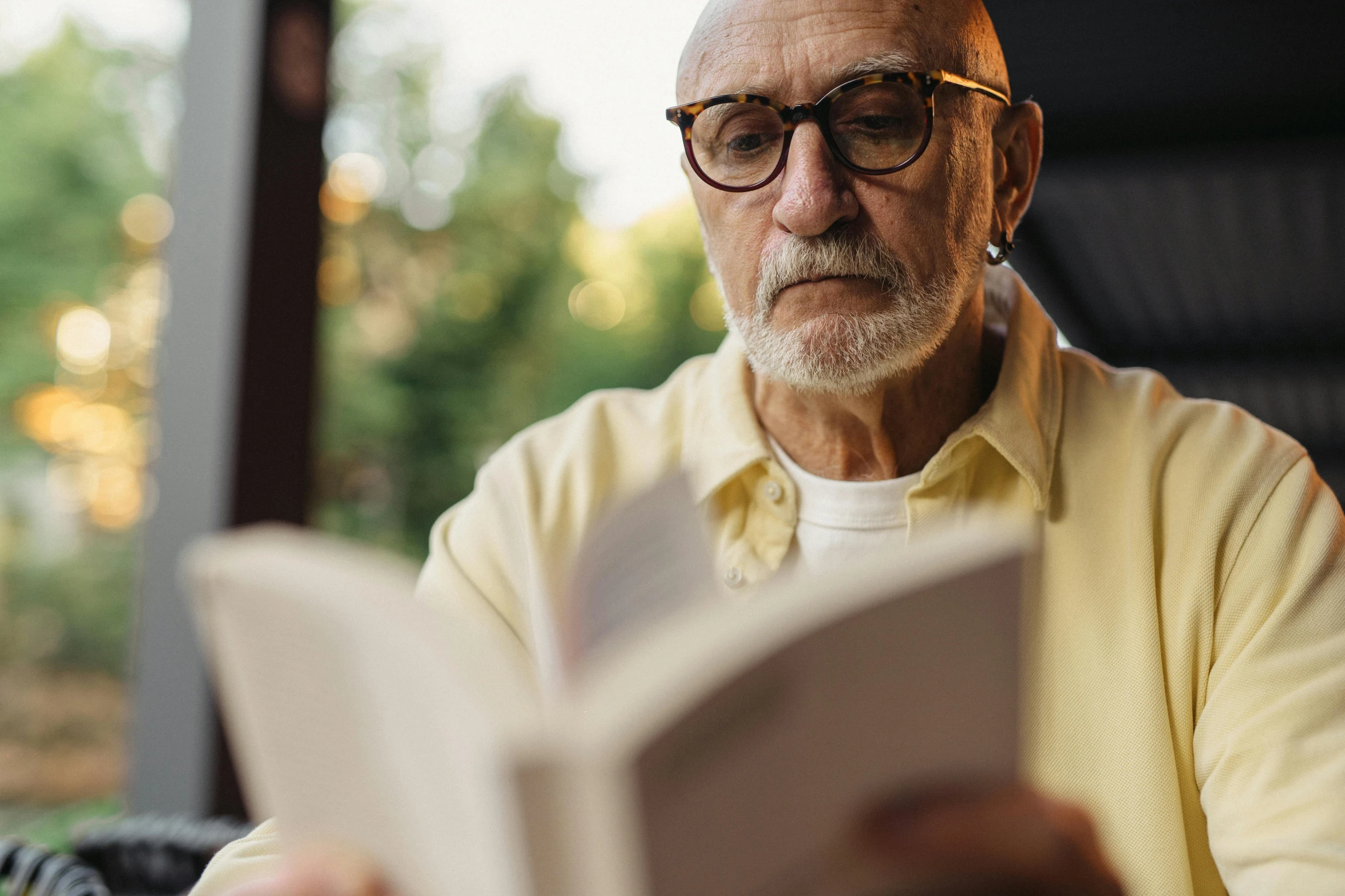 an elderly man reading a book in the shade