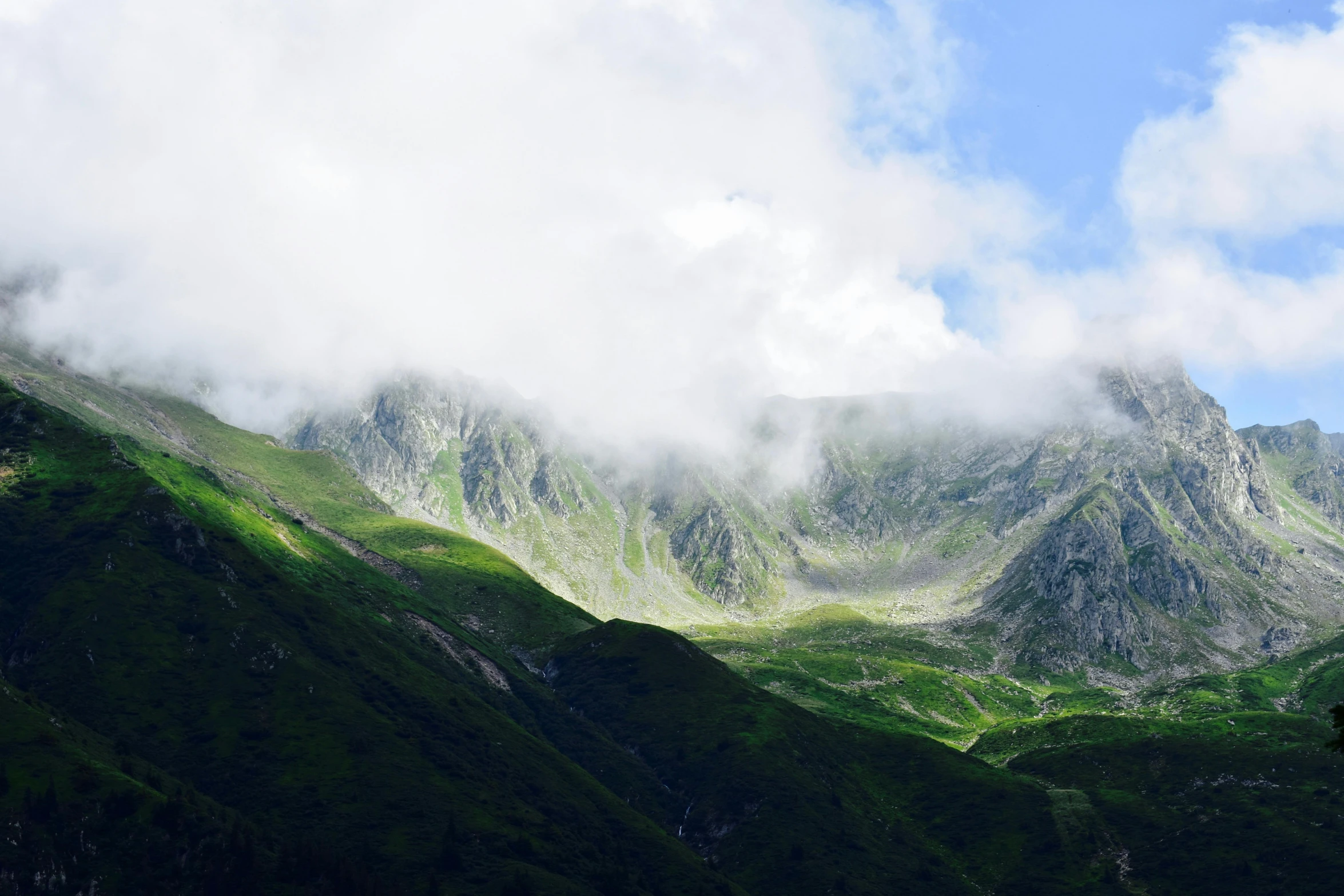 a couple mountains, each with clouds and a bird flying below