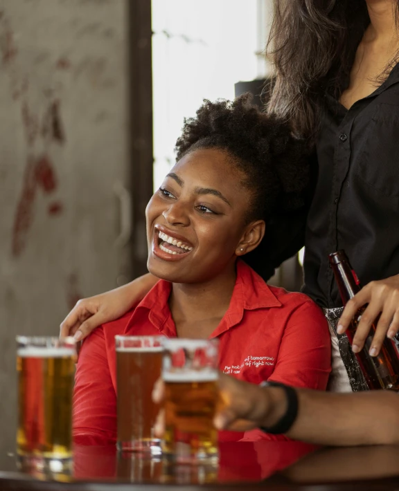 two women smile and hug while holding a glass of beer