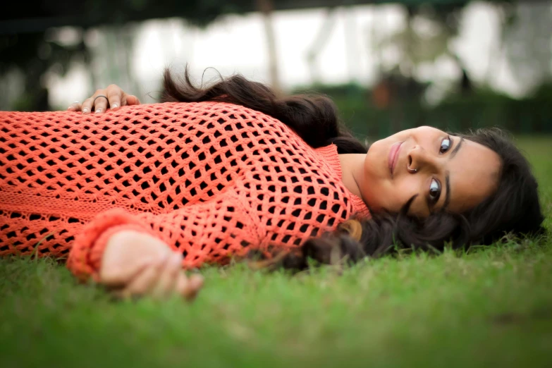 a young woman in an orange sweater lays in the grass