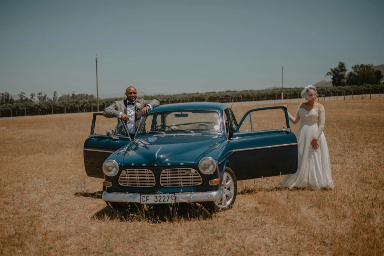 a bride and groom standing next to a car in a field