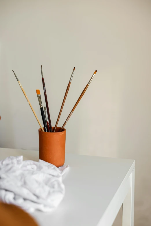 art brushes in a pot on top of a white table