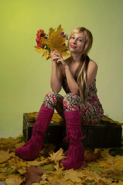 a woman sits in autumn leaves holding an up fall leaves