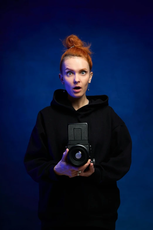 woman in black sweatshirt holding up an old camera