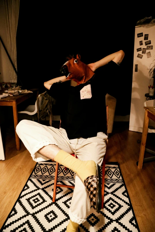 a man in black shirt sitting on chair with cow mask