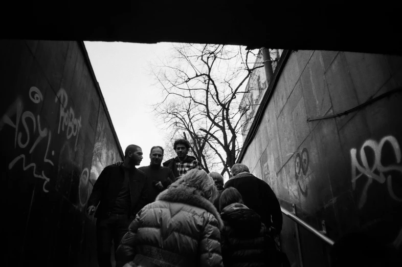 black and white pograph of people standing near a wall with graffiti