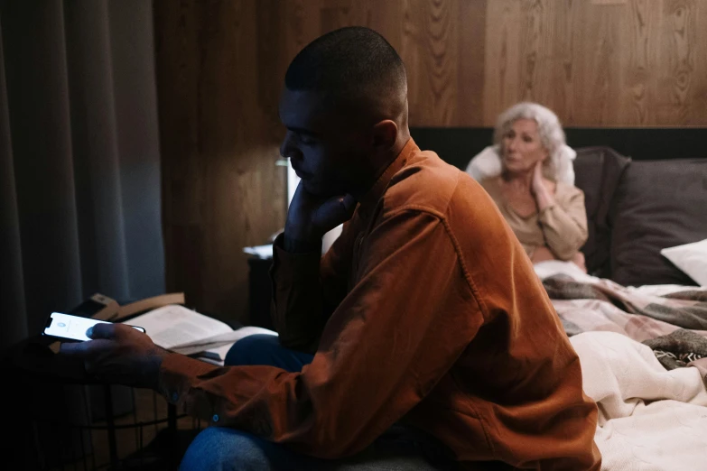 a woman on a cellphone sits next to a man on a bed