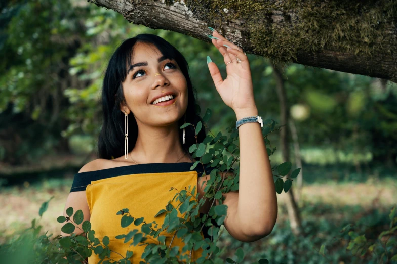 a woman standing under a tree and reaching up to the nch