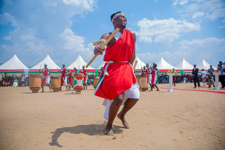 a man in a red robe, in front of some people and drums