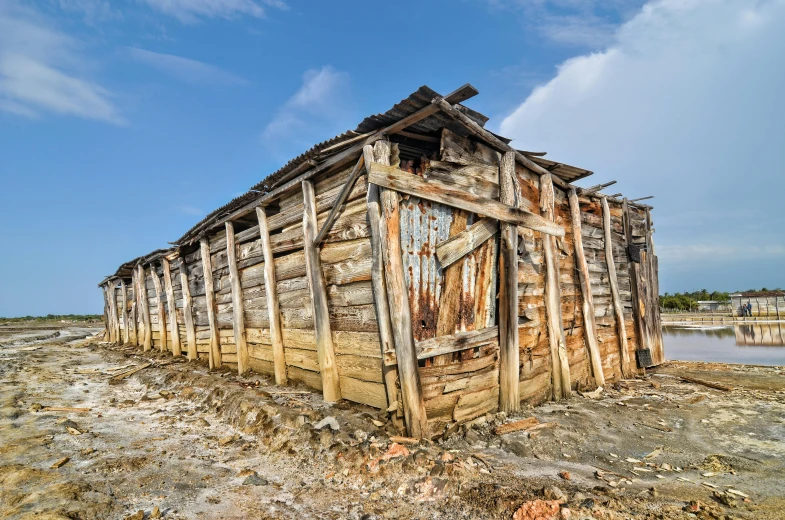 old wooden shack, leaning against wooden slats, stands alone in the middle of dry ground