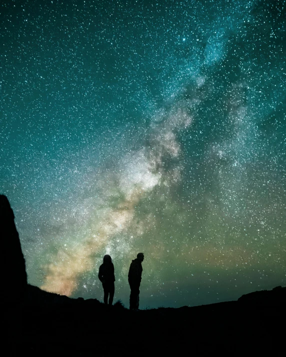 two people stand in front of the stars of a sky filled with bright lights