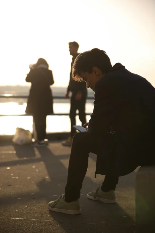 man looking at his cell phone while others stand on the shore