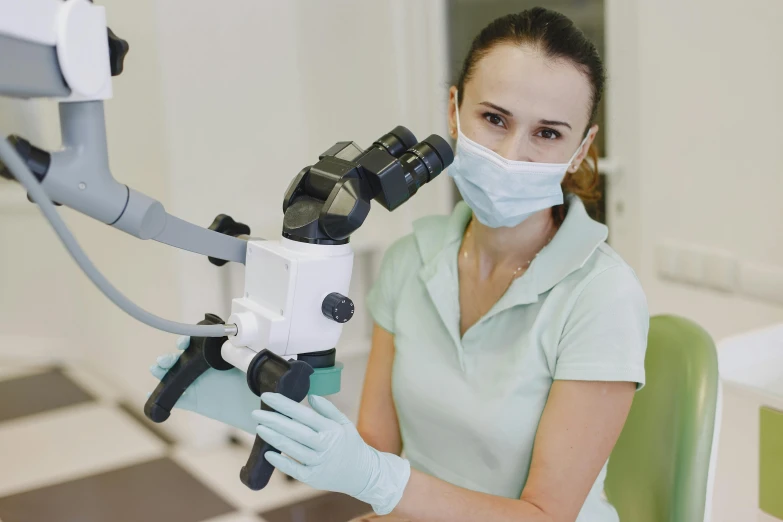 a woman with a mask and gloves holding microscope equipment