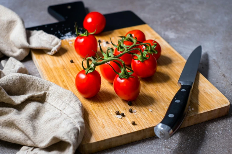 some red tomatoes sit on a  board next to the knife