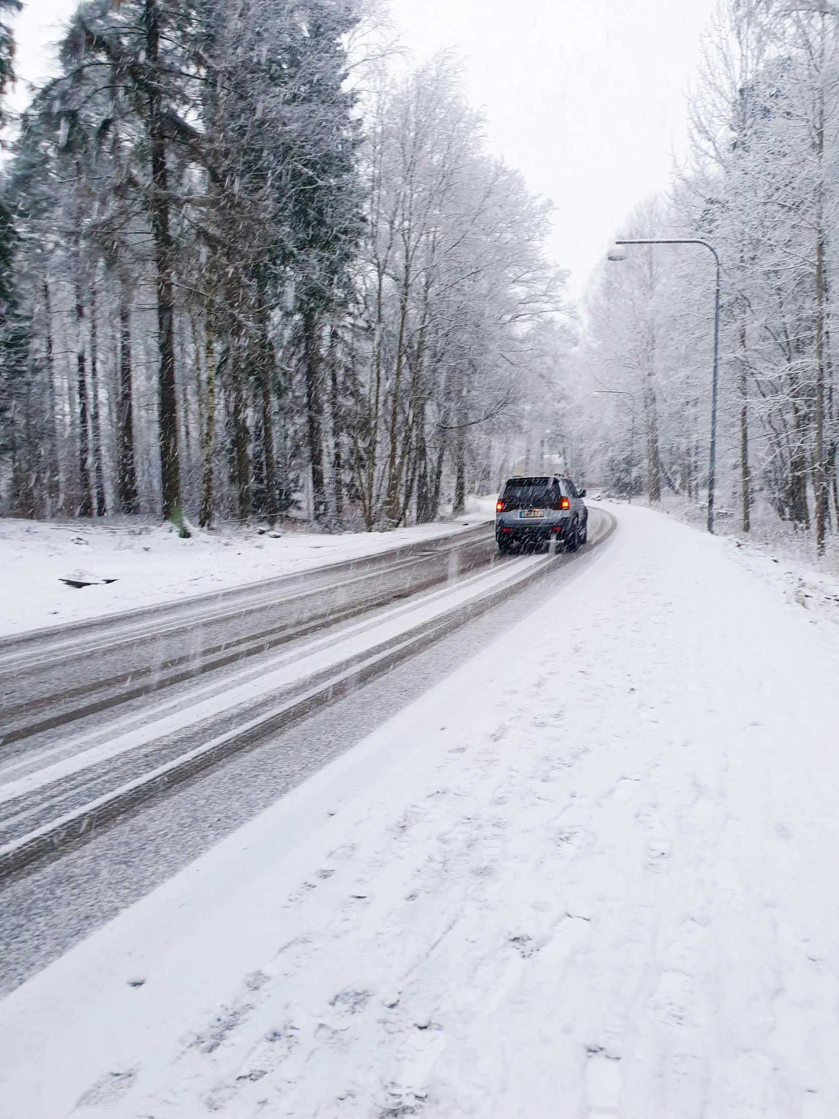 a car drives down the road, and it's snowing