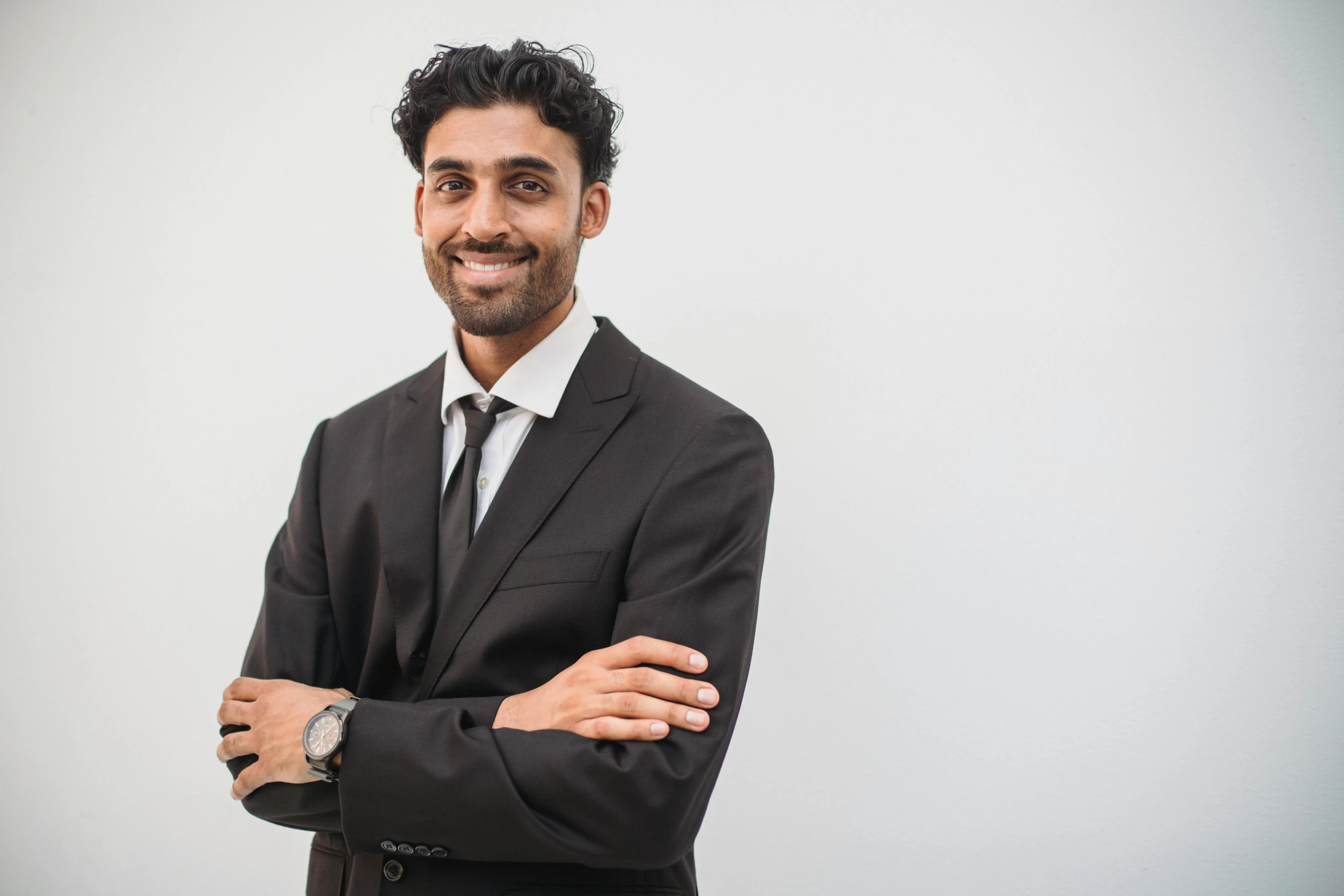 a smiling man in a suit standing with his arms folded