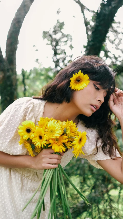 young lady wearing white and holding yellow sunflowers in an outdoor setting