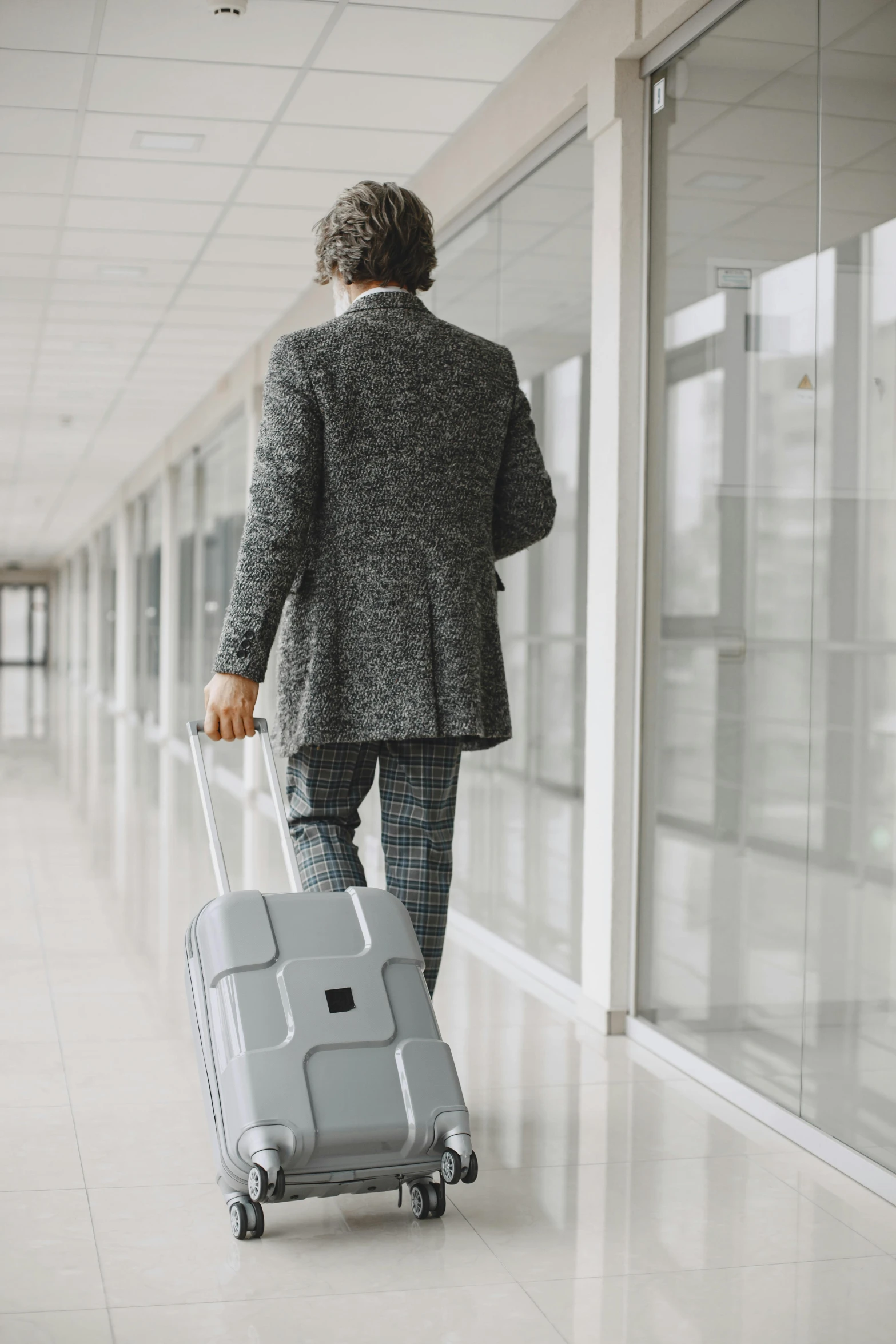 man with a suit coat holding a suitcase walking down an airport corridor